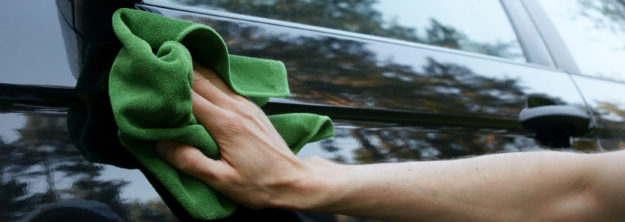 Clean-Car Hand using a green cloth to polish a black car door.