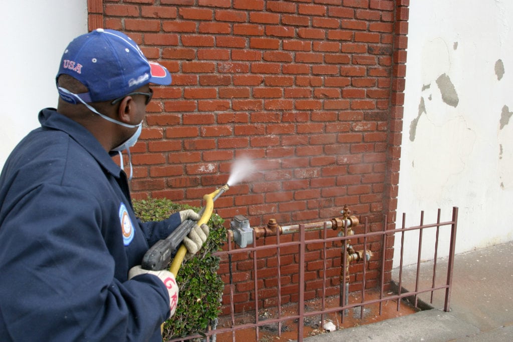 A man cleaning graffiti from a brick wall with a pressure washer.