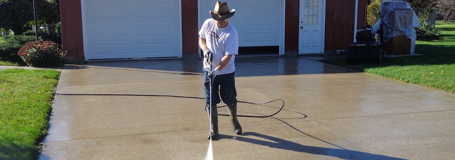 Man cleaning oil from a driveway with a pressure washer.