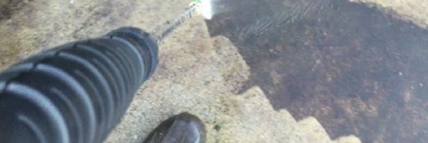 A man pressure washes dirt off a pavement. A man pressure washes dirt off a pavement.