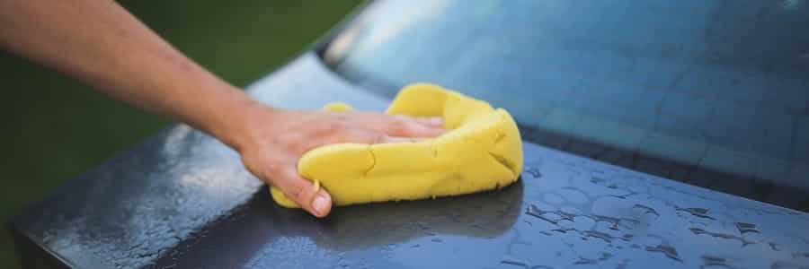 A hand washes a black car with a towel