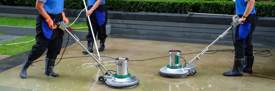 Three men cleaning an exterior floor with floor scrubbers.