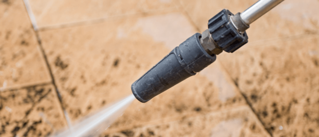 Pressure Washer Mainteance Tips Close-up of a pressure washer nozzle spraying water on a dirty tiled surface.