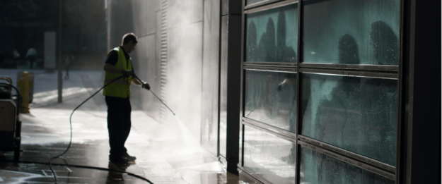 can you pressure wash windows (1) A person wearing a high-visibility vest power washing the exterior surface of a modern building.