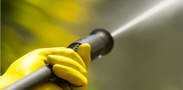pressure washer remove paint (1) A person wearing yellow rubber gloves holding a high-pressure hose spraying water.