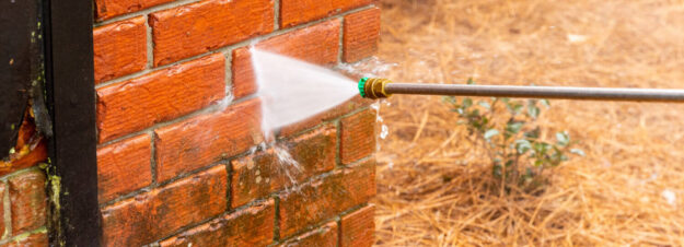 pressure washing bricks dos donts Close-up of a pressure washer cleaning a red brick wall.