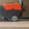 Person operating a floor cleaning machine on a light-colored wooden floor.