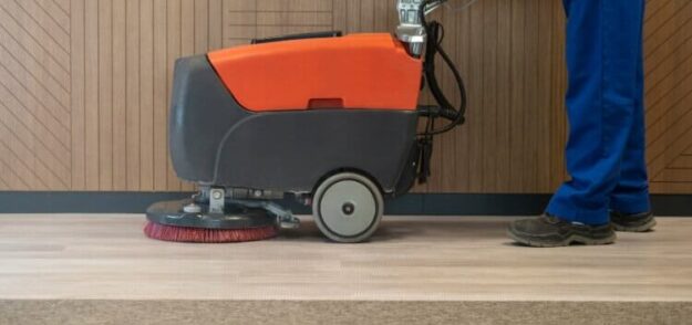 floor scrubbers & carpet Person operating a floor cleaning machine on a light-colored wooden floor.