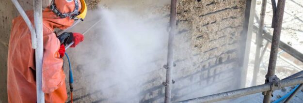pressure washers in construction (1) Worker in orange protective clothing and helmet using a power washer on a building facade surrounded by scaffolding.