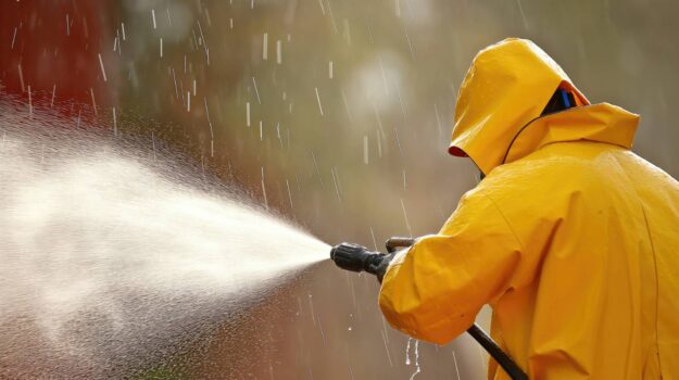Importance of Personal Protection Equipment When Pressure Washing Worker wearing PPE while pressure washing outside.