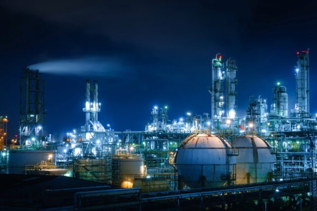 Importance of Cleaning Heavy-Duty Equipment in the Chemical Industry Industrial plant at night with illuminated towers and large spherical storage tanks against a dark sky.