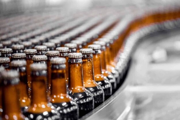 The Role of Pressure Washing in the Food & Beverage Industry Rows of brown glass bottles with metal caps on a conveyor belt in a bottling factory.