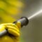Close up of a yellow-gloved hand holding a pressure washer sprayer.