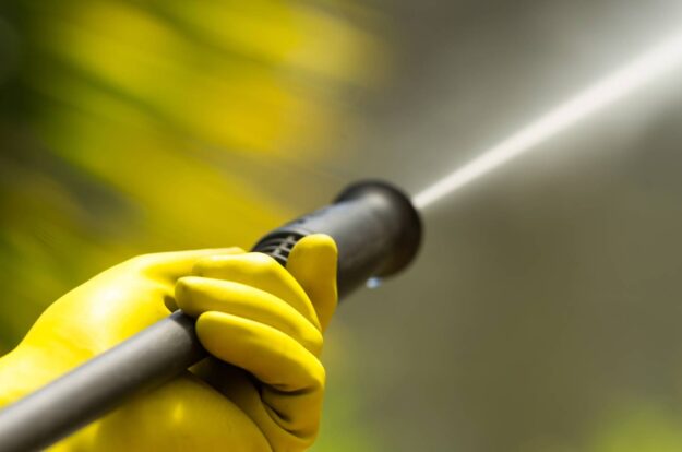 Industrial-Grade Pressure Washers vs. Consumer Models: What’s the Difference? Close up of a yellow-gloved hand holding a pressure washer sprayer.